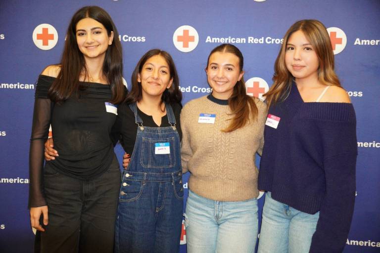 Four youth volunteers smile in front of a Red Cross backdrop.