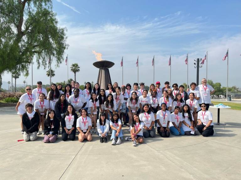 A group of about 50 Red Cross youth volunteers pose infront of American Flags and an olympic torch flame. 