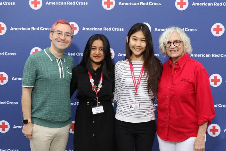 Four individuals smile infront of Red Cross backdrop.