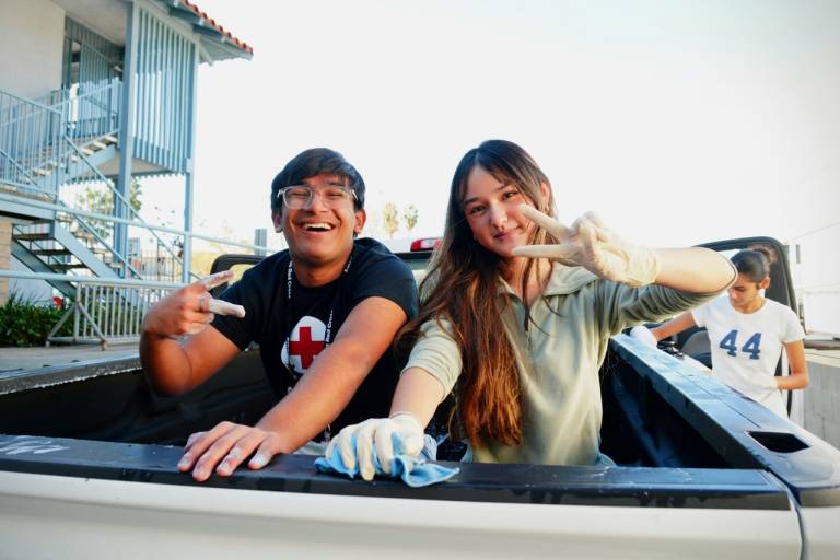 Two volunteers wash the bed of a Red Cross truck and smile and show peace signs.