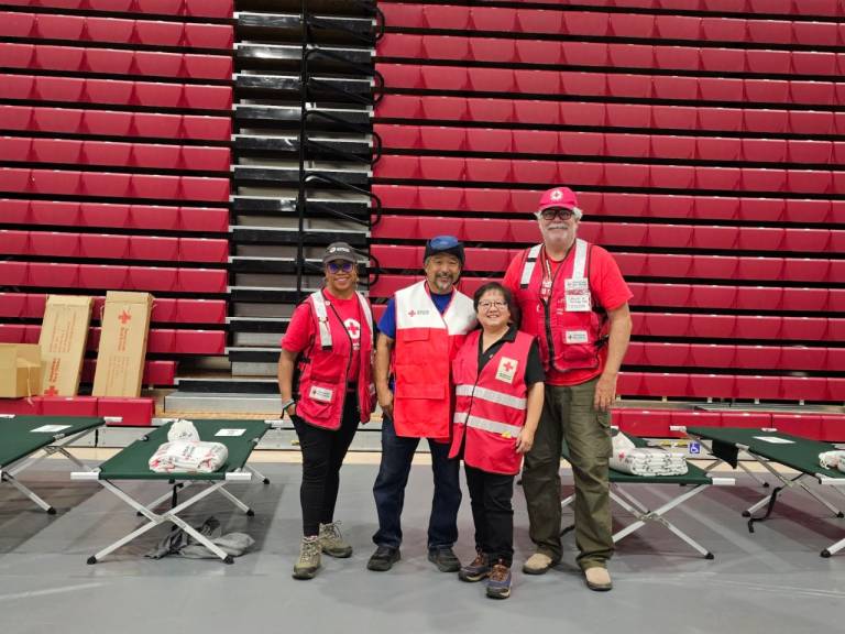 Group of four volunteers standing next to cots with blankets