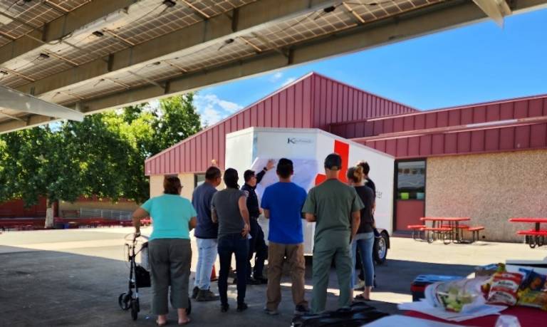 Group of people standing in front of Red Cross disaster trailer looking at a map