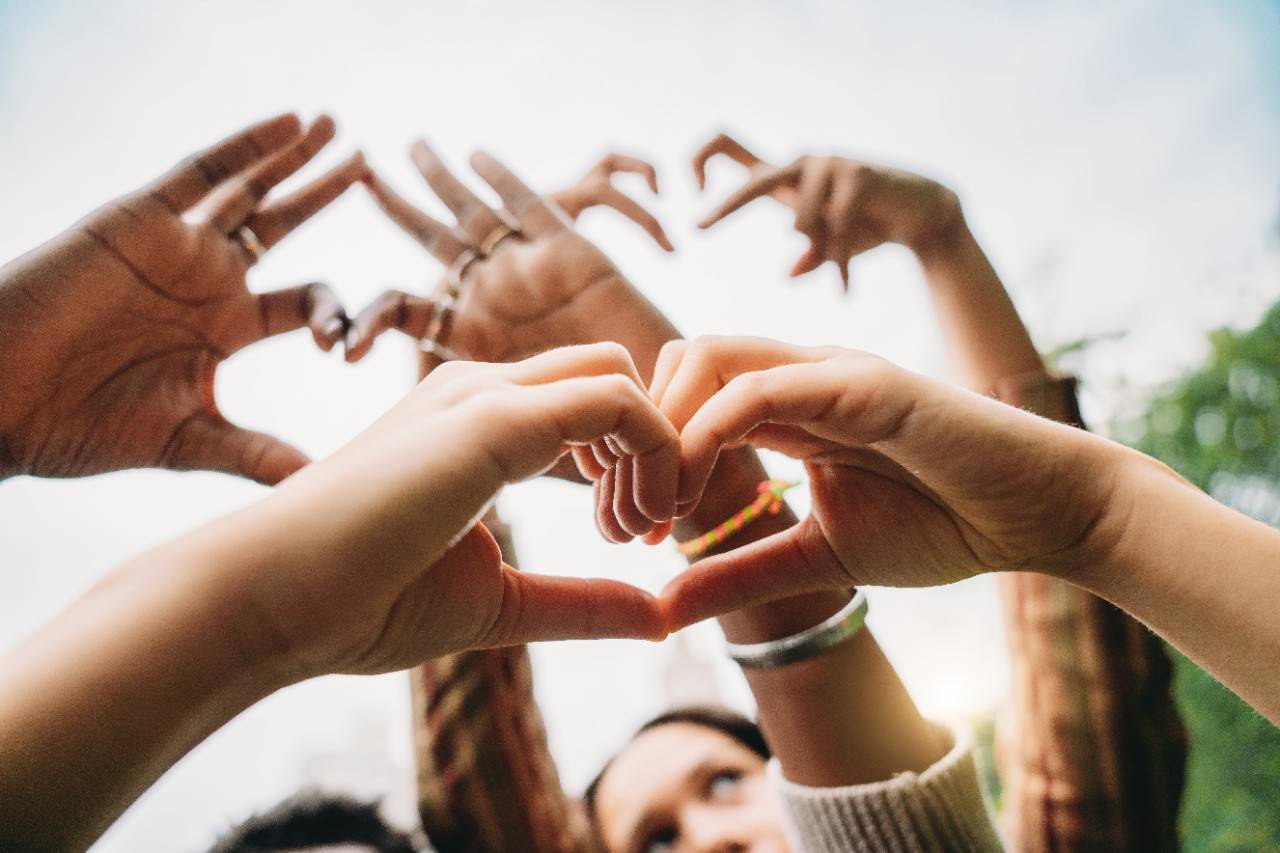 Conceptual shot of some hands making heart shapes with fingers. Sky in the background.