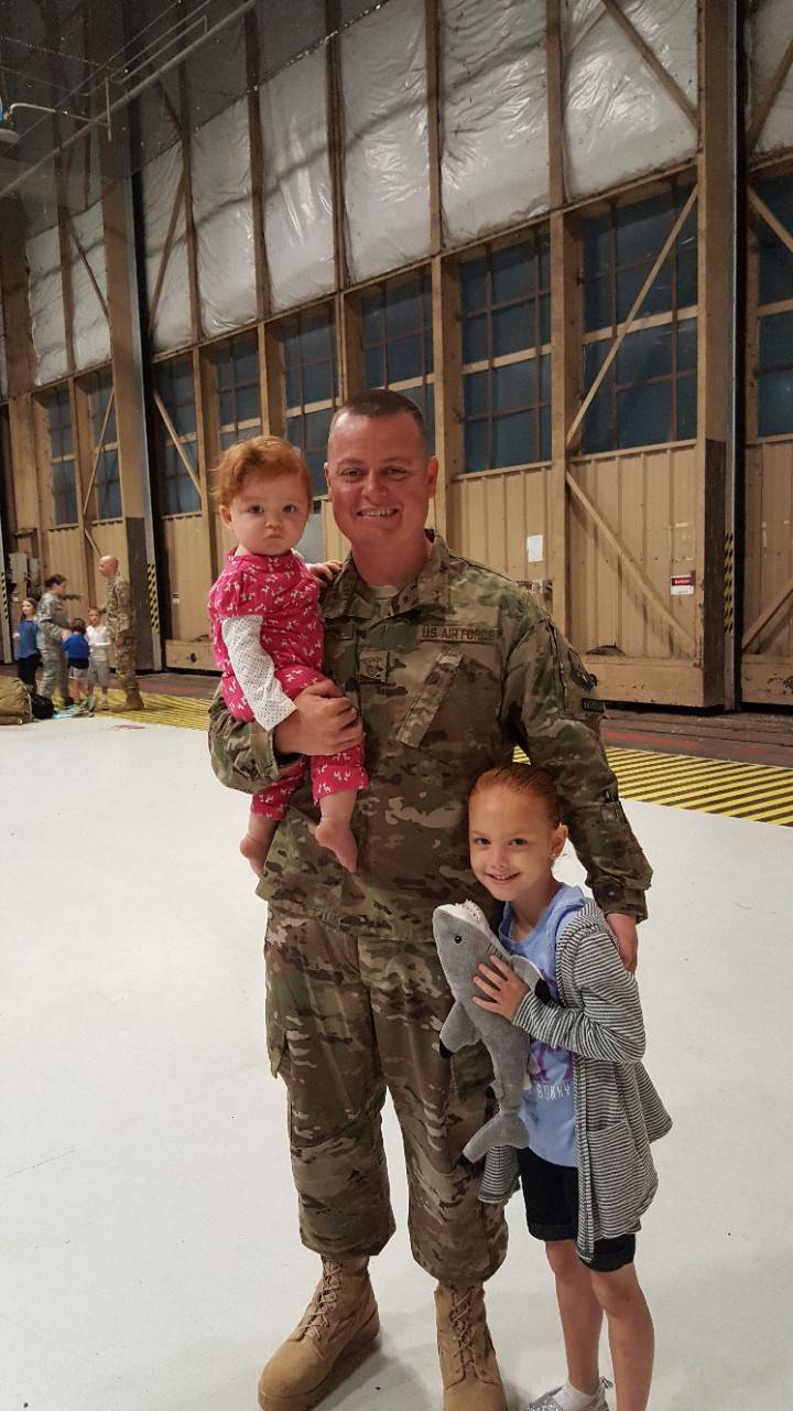 United Staets military member stands in uniform next to his two girls