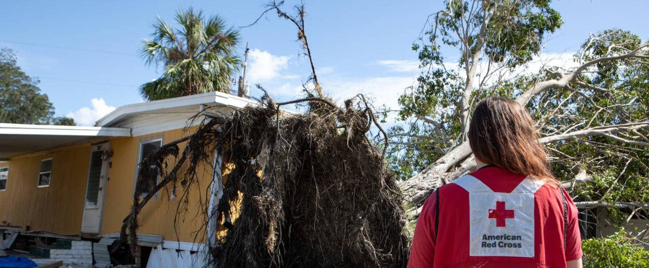 October 12, 2024. St. Petersburg, Florida.
American Red Cross Volunteer Taylar Sausen from Alaska stands in front of a home in the Twin Cities Mobile Home Community in St. Petersburg, Florida. This home and many others in this neighborhood saw devastating damage from both Hurricane Helene and Hurricane Milton. Neighbors told Red Cross Volunteers that this particular tree was still standing after Hurricane Helene but was brought down by the extreme winds of Hurricane Milton. Through the work with local partners and government agencies, the Red Cross is working to provide comfort, care and hope to this community and the many others like it as they work to recover from these major disasters. 
Photo by Marko Kokic/American Red Cross

