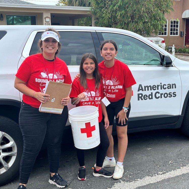 Three red cross volunteers; a woman and two young girls; girl holding red cross bucket