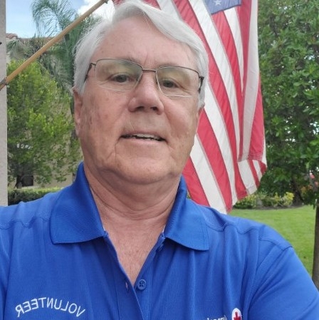 Dennis Parker in blue shirt with American flag behind him