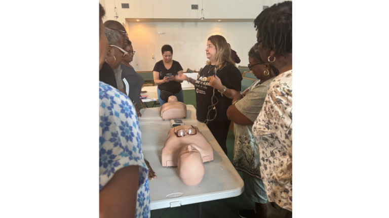 People agthered around a CPR instructor and mannequin