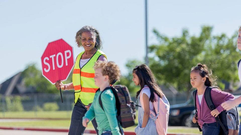 a school crossing guard holding a stop sign while children walk across the street.