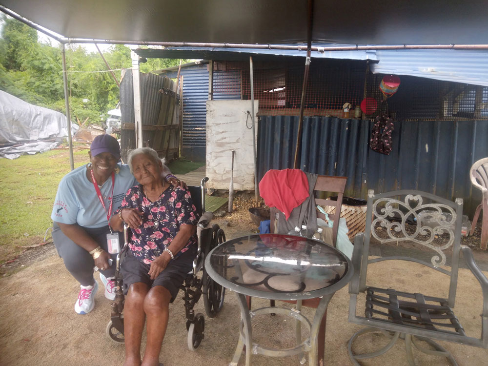 Elnita Barnett squtting down next to an eldery woman sitting in a wheelchiar.
