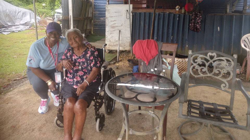 Elnita Barnett squtting down next to an eldery woman sitting in a wheelchiar.