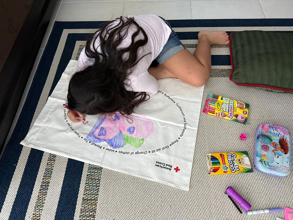 Young girl drawing on a large Red Cross coloring cloth with crayons.