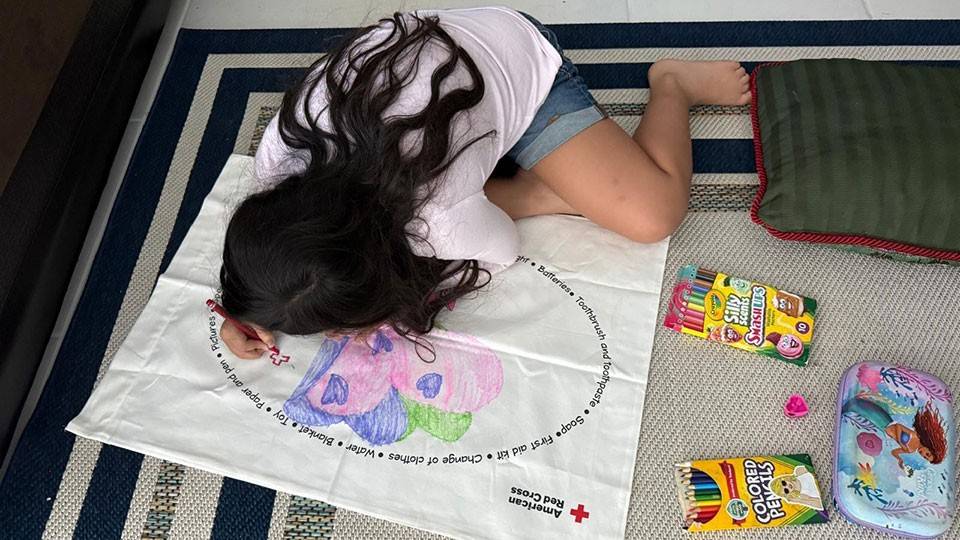 Young girl drawing on a large Red Cross coloring cloth with crayons.