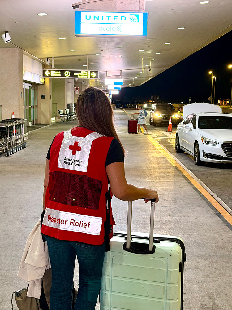 a Red Cross volunteer at the entrance of an airport at night with luggage in hand.