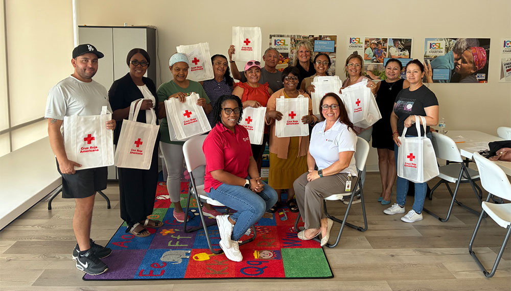 a group of people in a room holding up Red Cross preparedness kits.