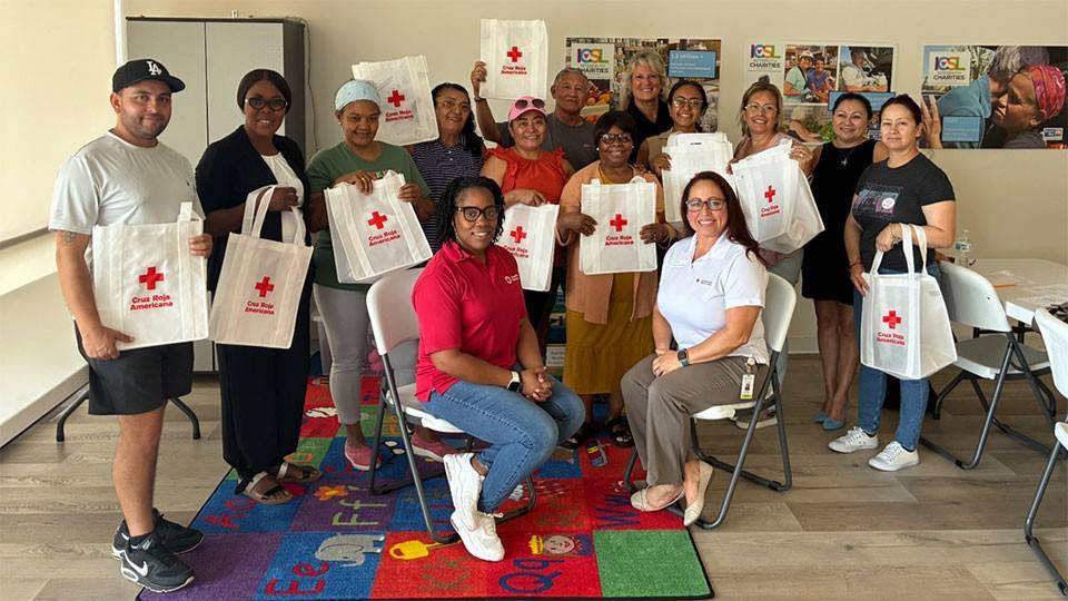 a group of people in a room holding up Red Cross preparedness kits.