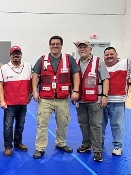Red Cross volunteer, Pete Suarez standing next to three other volunteers in a Red Cross shelter.