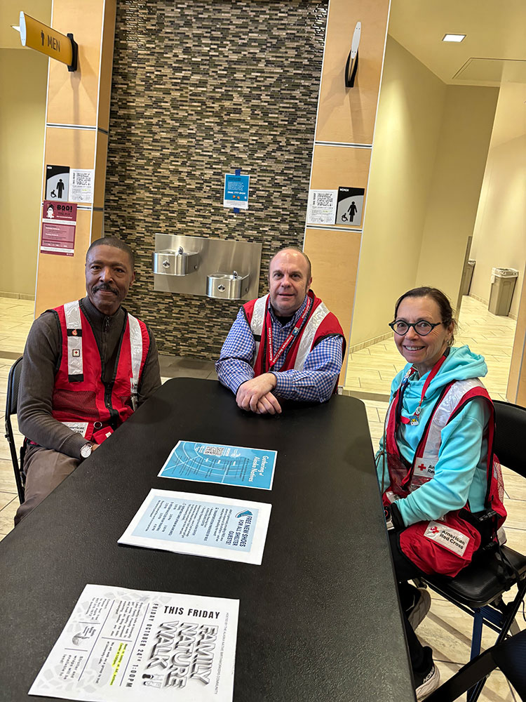 three Red Cross volunteers sitting at a table that has papers on it.