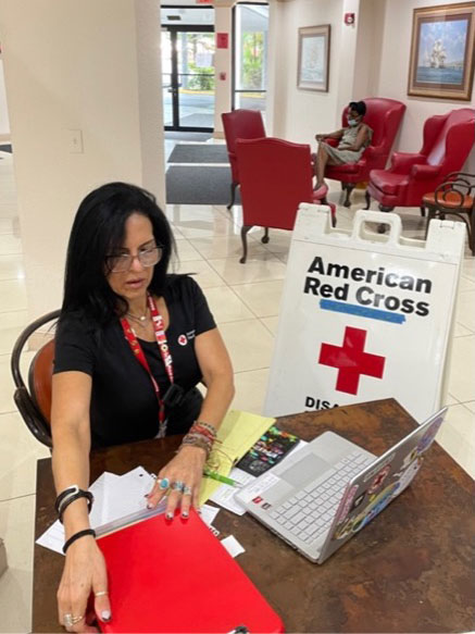 Red Cross volunteer, Suzy Rodriguez sitting at desk in a Red Cross shelter.