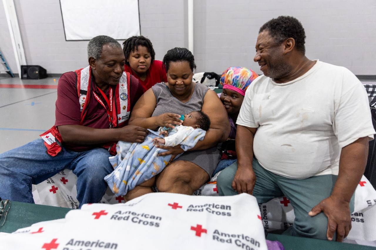 September 1, 2023. Valdosta, Georgia.
Red Cross disaster responder, Randolph M. Scott, meets the newest addition to Reginald and Angel Turner’s family at a Red Cross shelter in Valdosta, Georgia. The Turners, and their three children, sought refuge in an emergency shelter after their home was left unlivable by Hurricane Idalia’s strong winds and devastating storm surge. Due to the climate crisis, hurricanes are becoming more intense and destructive with higher rainfall and storm surges.
Photo by Scott Dalton/American Red Cross