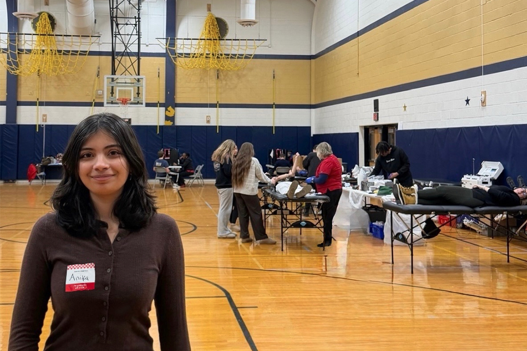 Anika Harris stands in a gymnasium with a blood drive going on in the background. 
