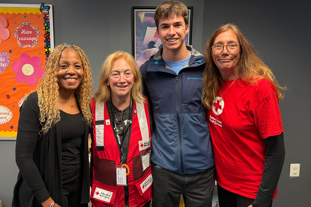 Photo of 4 people standing with the arms around each other. two are wearing Red Cross shirts.