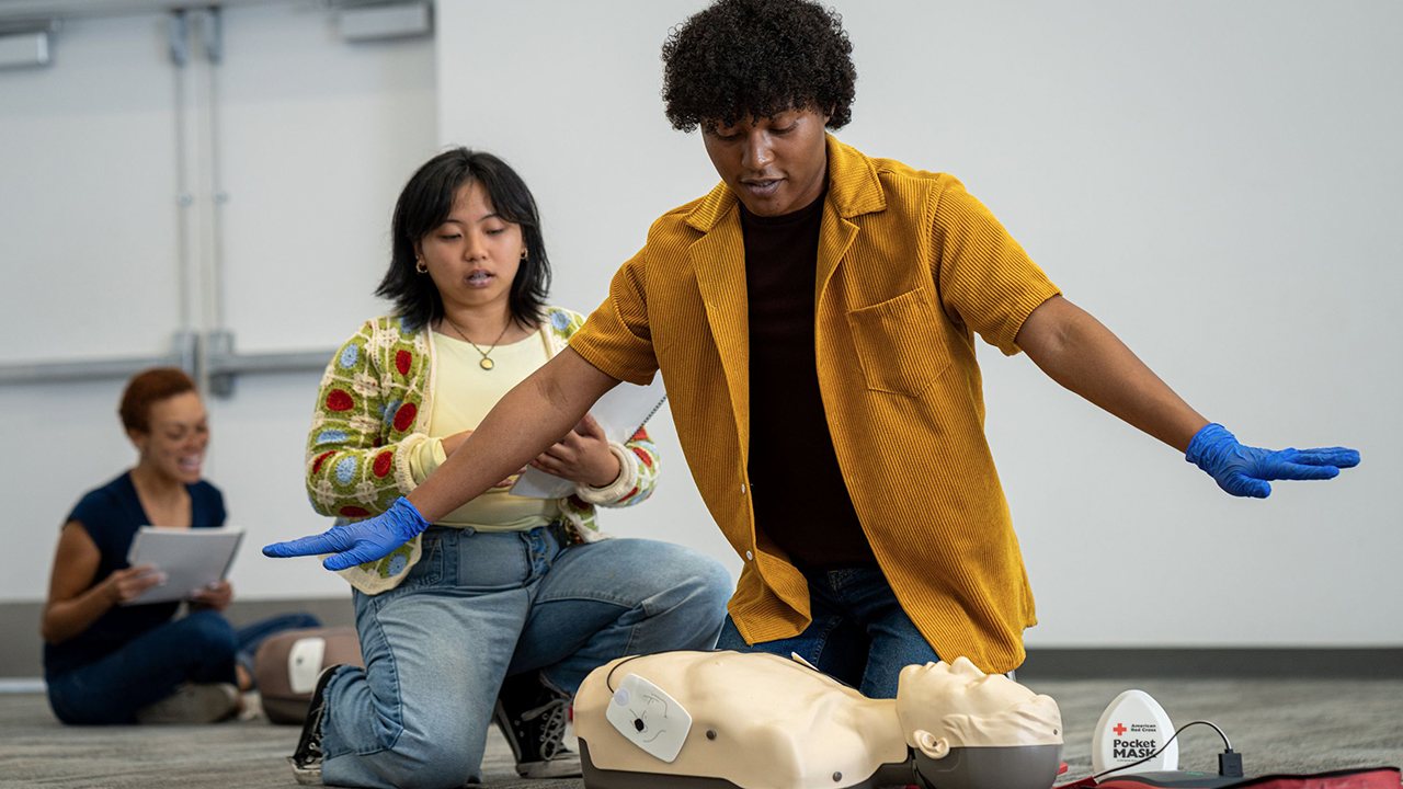 Photo of a young man and woman practicing CPR with a manaquin. 