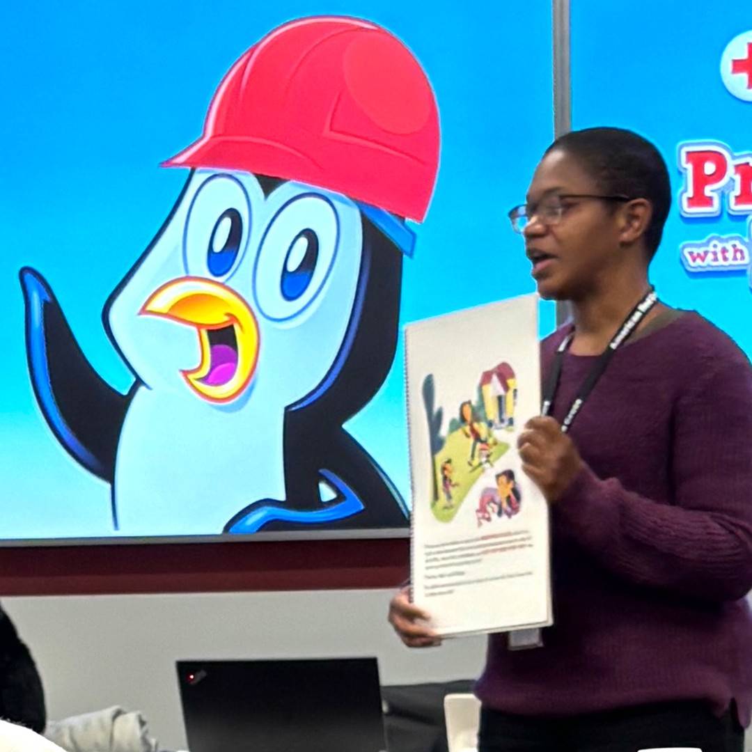 Photo of an Black adult woman holding oversized graphic and standing in front of a cartoon penguin graphic.