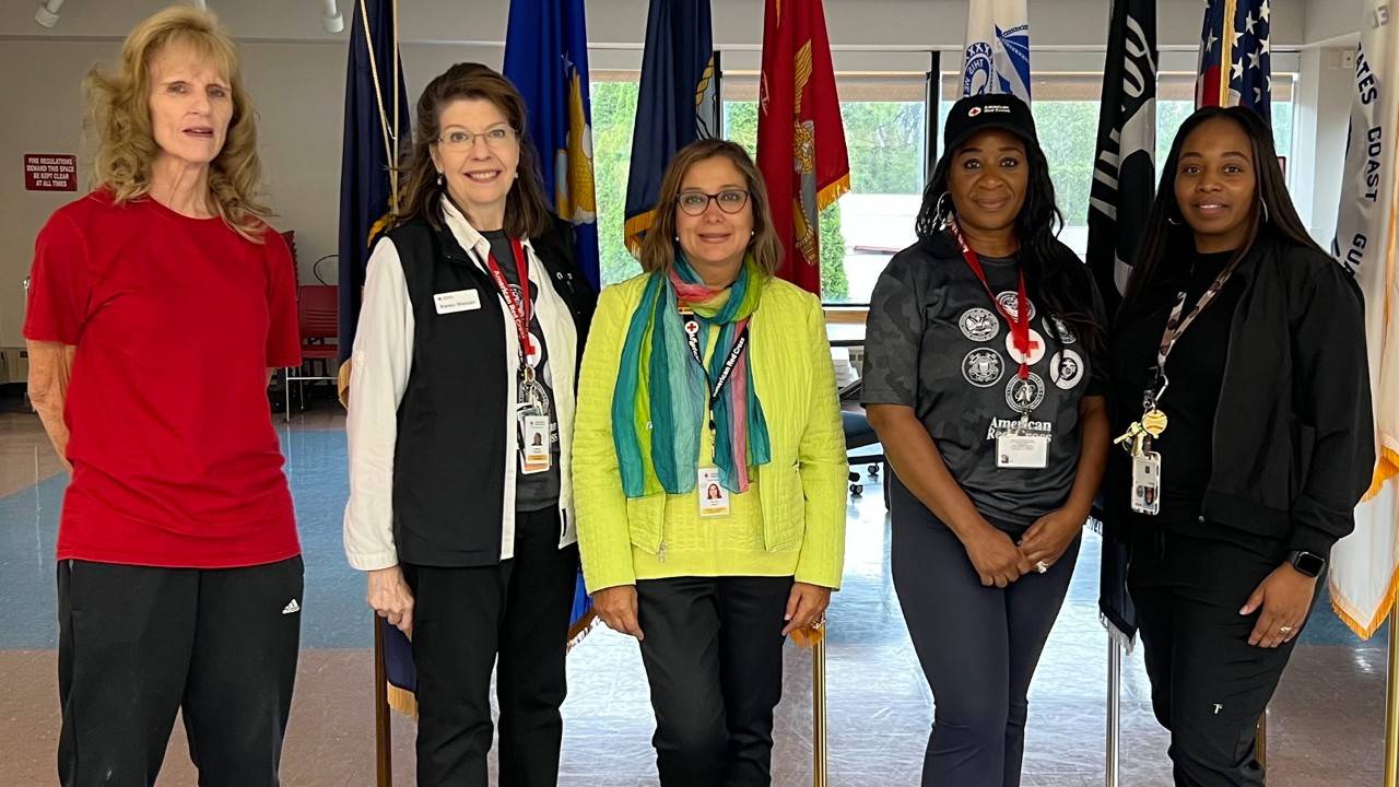 Five adult women stand in front of several flags.