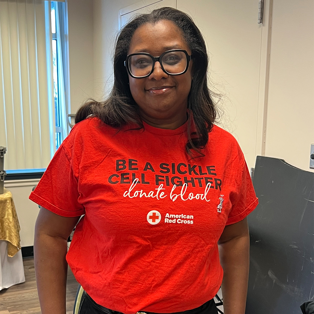 Photo of Dana Walters wearing a red T-shirt that reads Be a Sickle Cell Fighter, donate blood.