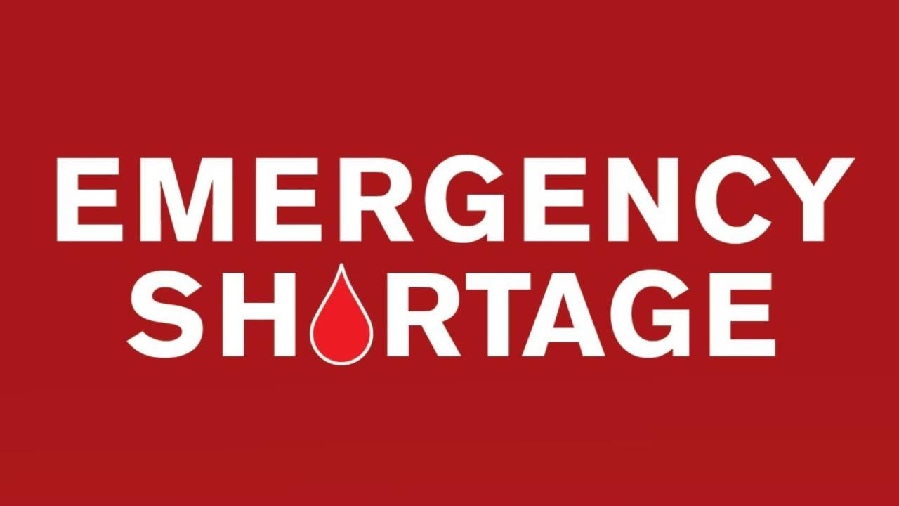 Graphic with a solid red background displaying the words “EMERGENCY SHORTAGE” in large white capital letters. A red blood drop icon outlined in white replaces the letter “O” in the word “SHORTAGE,” emphasizing an urgent need for blood donations.