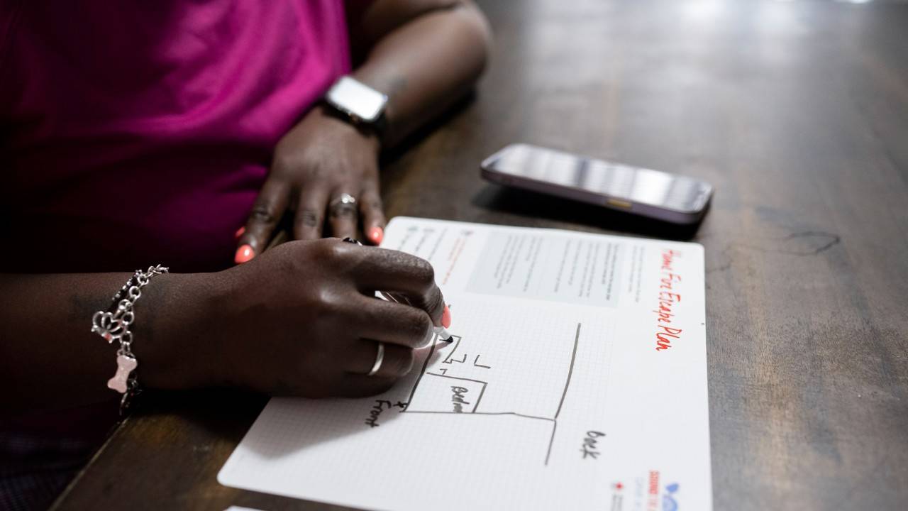 A person sitting at a table with hands folded, reviewing a printed home fire escape plan document with a sketched home layout.