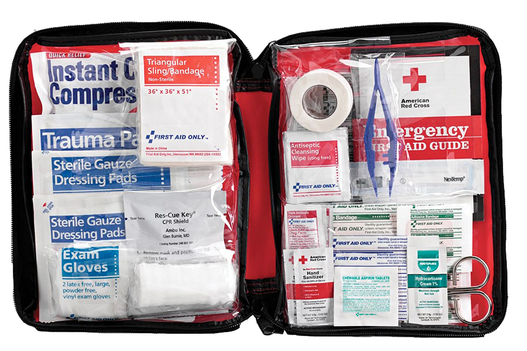 Open black zippered American Red Cross Ready First Aid Kit filled with organized medical supplies, including trauma pads, sterile gauze, exam gloves, CPR shield, bandages, antiseptic wipes, and medical scissors.