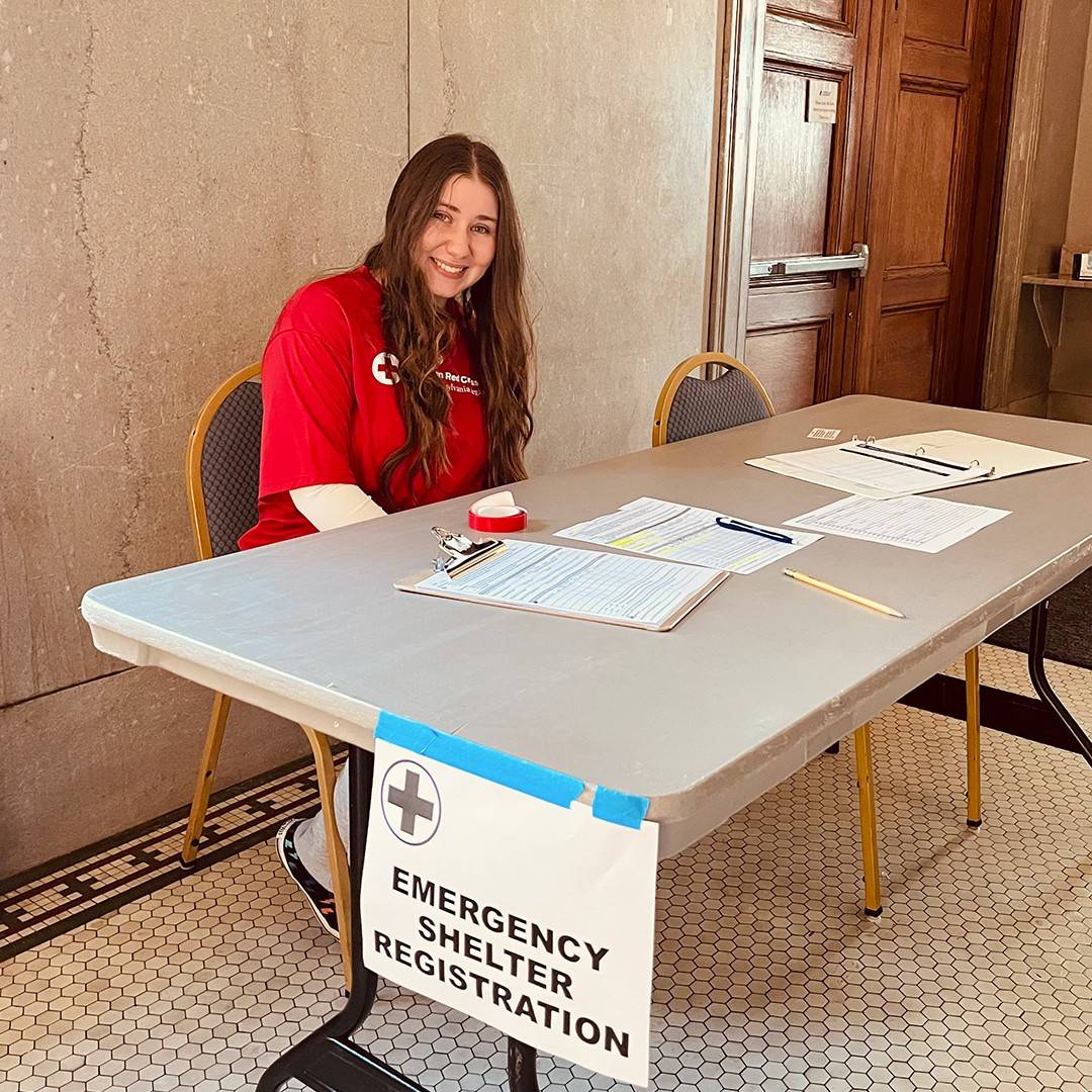 Immaculata University student Francesca Giardidi sits at a table with a sign attached that reads: Emergency Shelter Registration