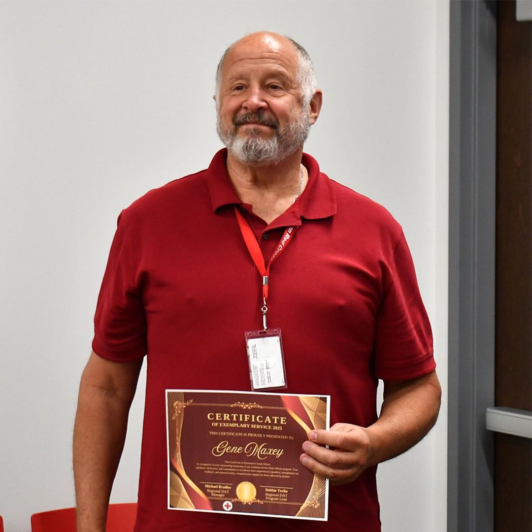 American Red Cross volunteer Gene Maxey smiling while holding a framed "Certificate of Exemplary Service 2025" award presented in his name.