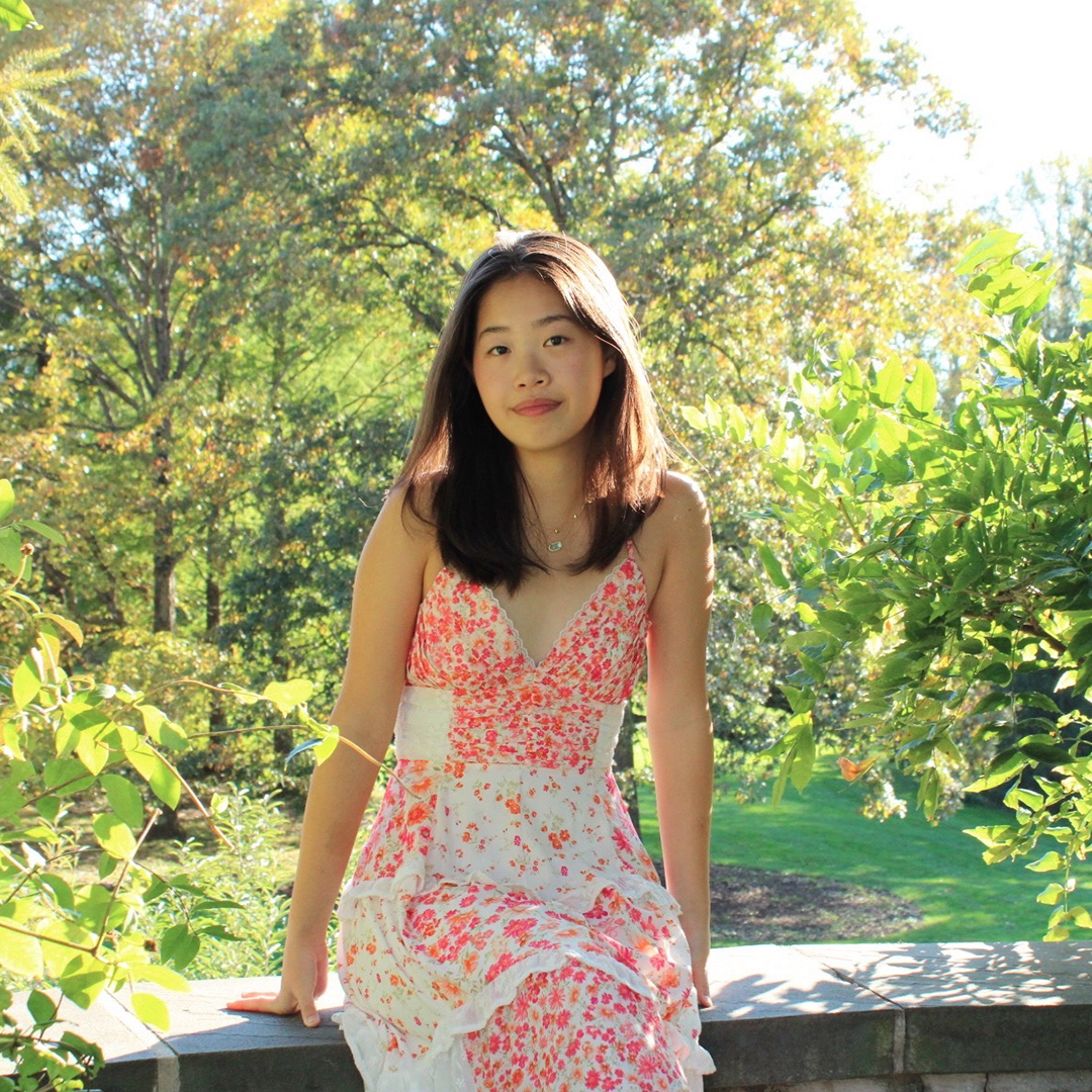 Haeun Cho smiling and standing outdoors in a sunlit garden, wearing a pink floral dress.