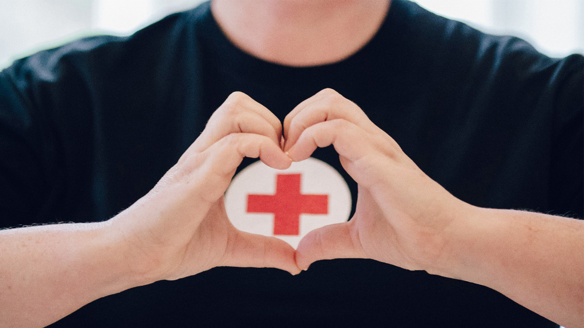 Person making a heart with their hands in front of the Red Cross logo on their shirt.