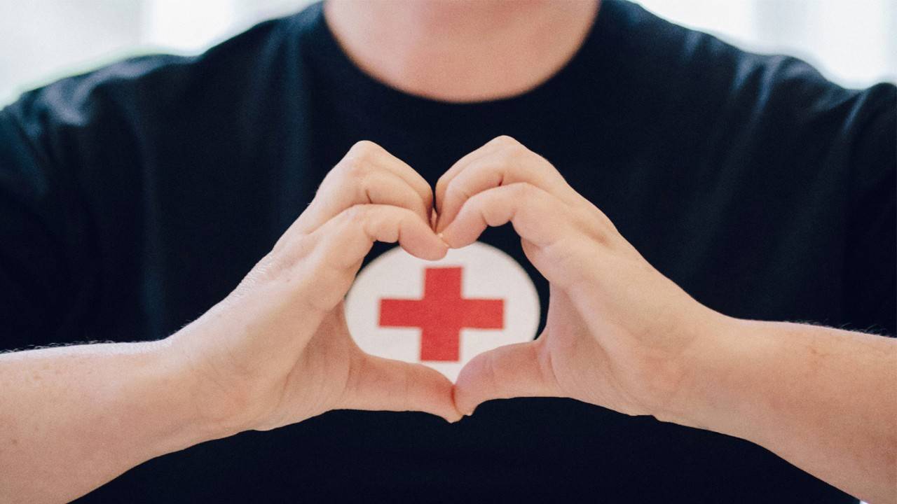 Person making a heart with their hands in front of the Red Cross logo on their shirt.