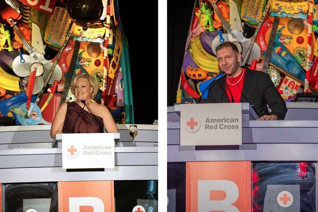 Photo of Jennifer Graham on the left and Lee Farrell on the right. They are standing at a podium at base of the Statue of Liberty arm and torch replica made from toys.