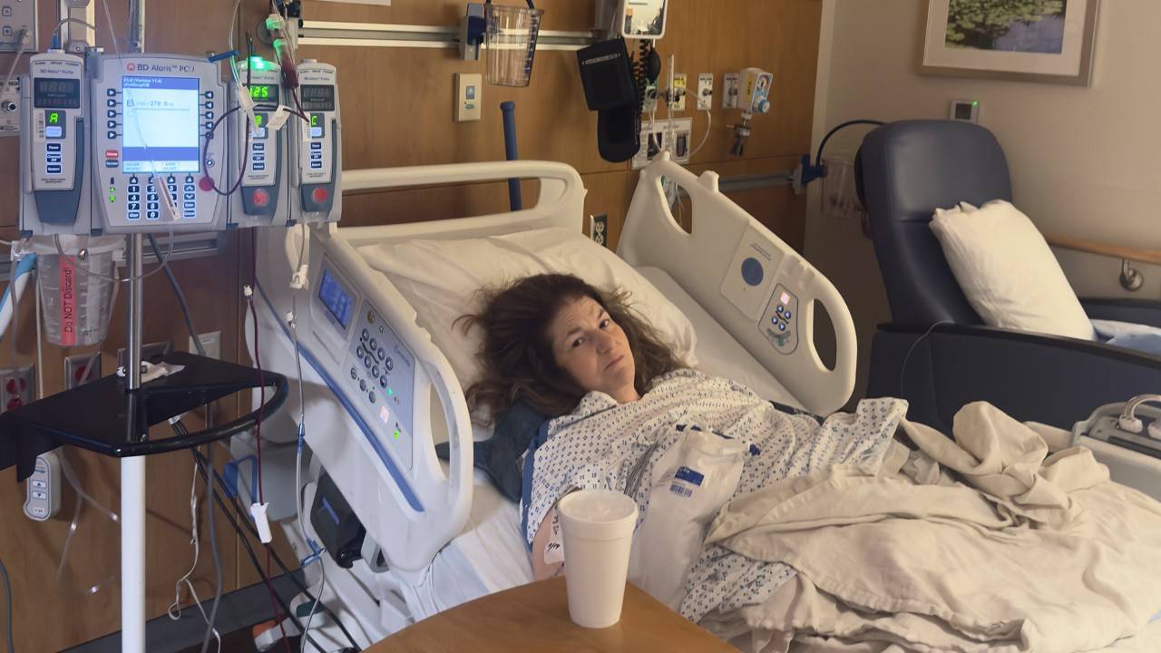 Photo of a woman in a hospital bed with a blood bag and IVs hanging next to her as she receives a blood transfusion.