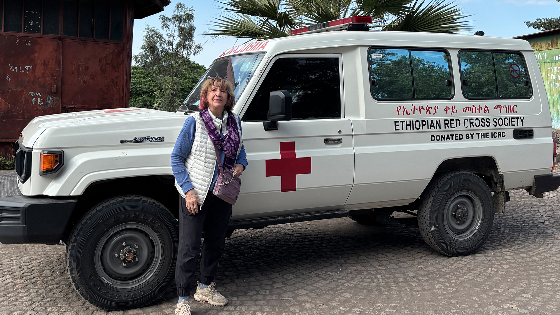 American Red Cross volunteer Judith Weeks stands alongside a white Ethiopian Red Cross ambulance with a red cross symbol on the door and the words "Ethiopian Red Cross Society" in English and Amraric.