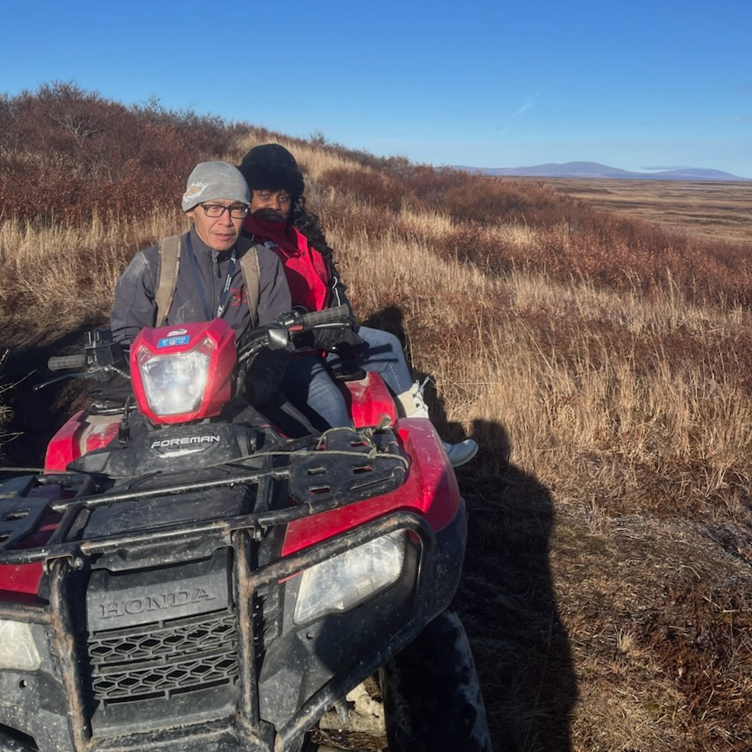 Lisa McGee rides on the back of an all-terrain vehicle in the Alasakan tundra.
