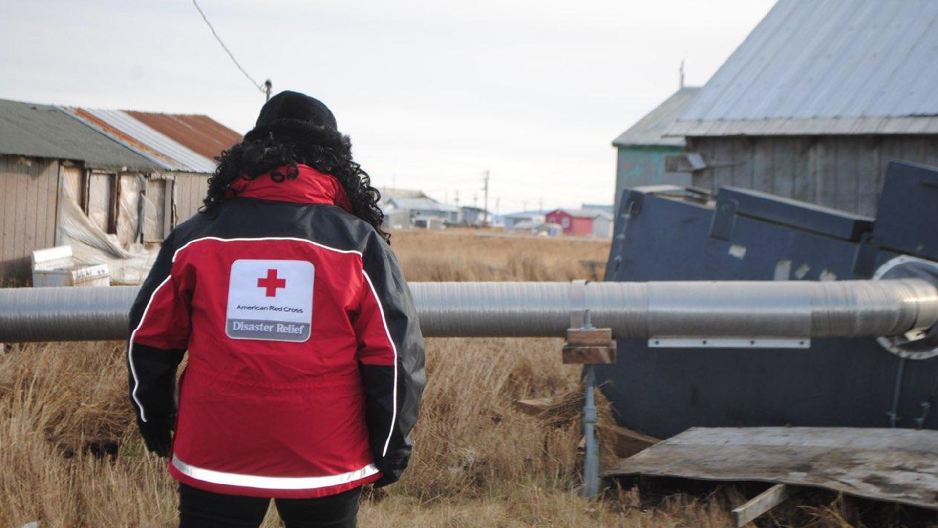 A woman wearing a Red Cross coat surveys damage in Alaska.