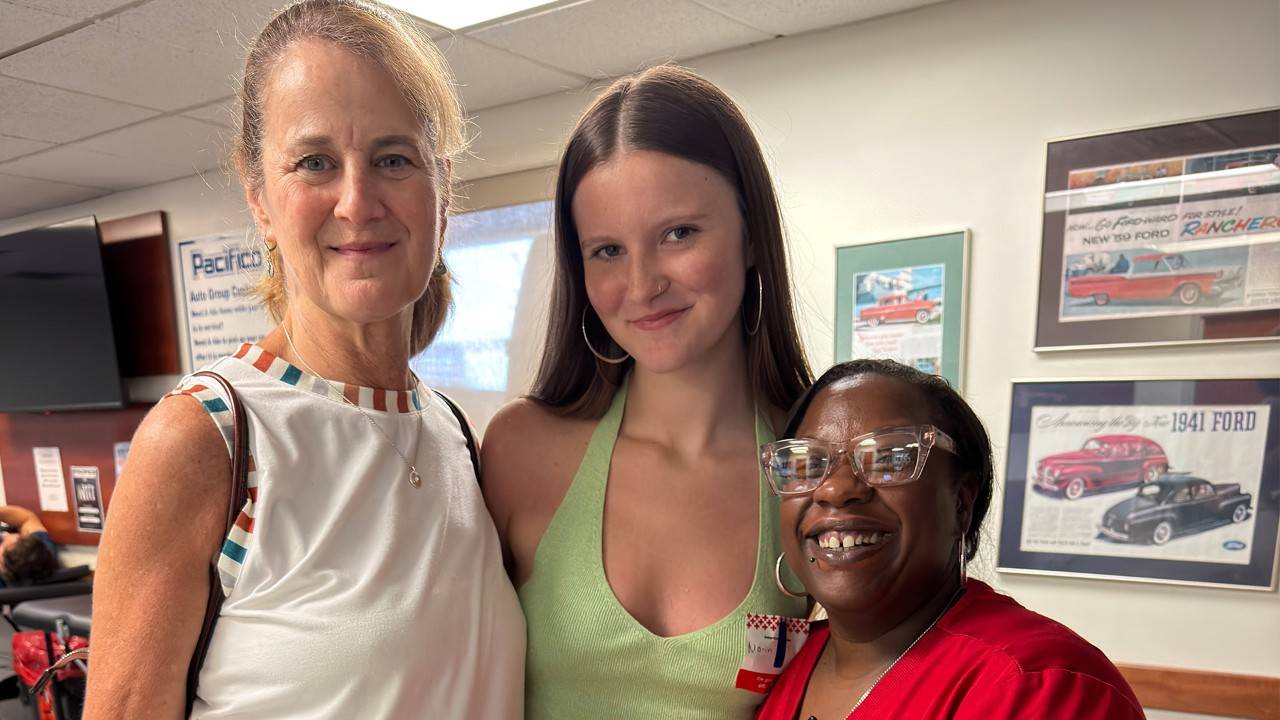 Maria Shankin, her daughter Marin, and Red Cross phlebotomist Ikea Smith smile together at a blood drive.