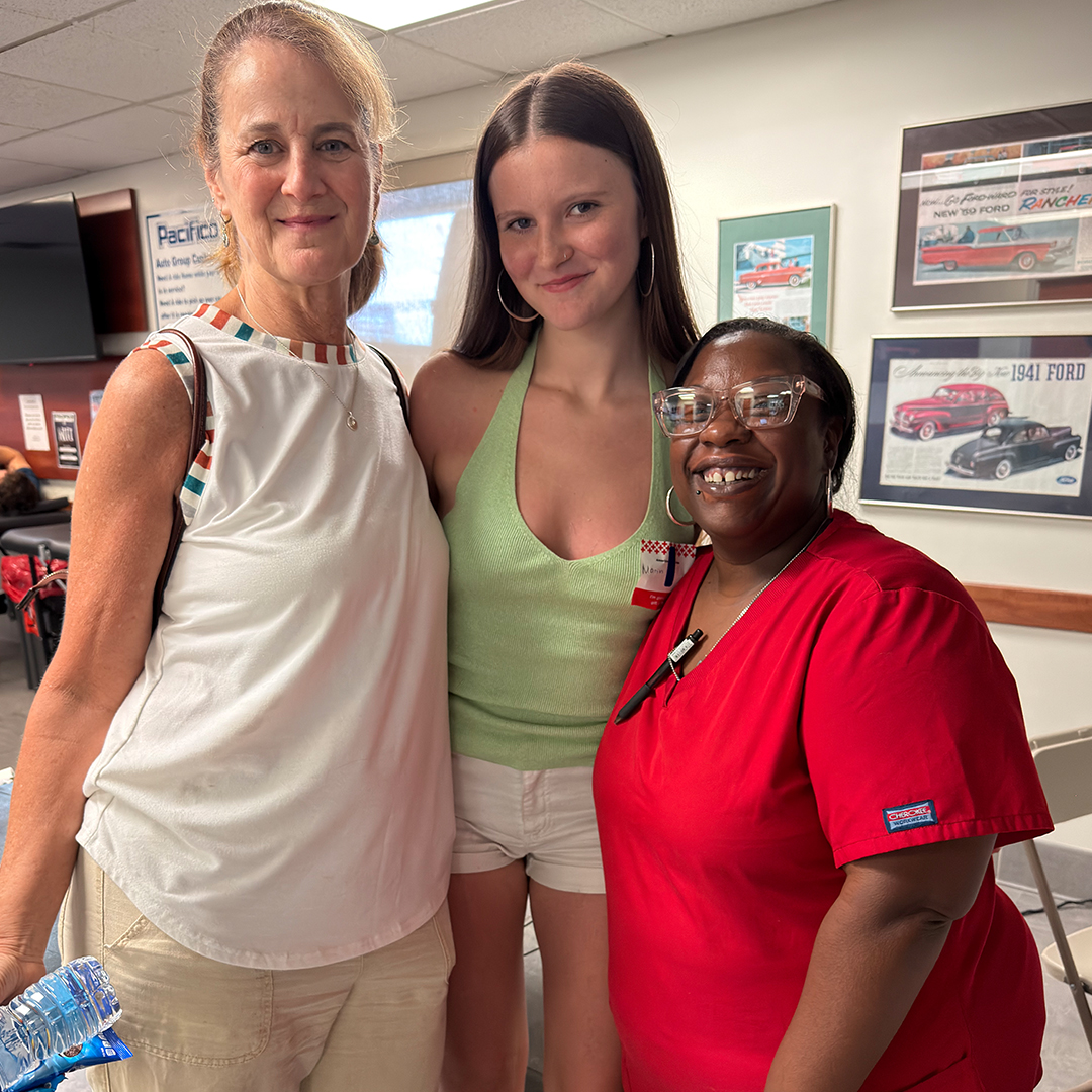 Maria Shankin, her daughter Marin, and Red Cross phlebotomist Ikea Smith smile together at a blood drive.