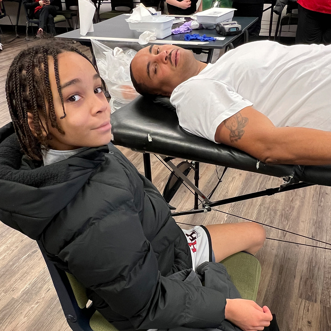 Photo of Maurice Williams on a blood donation cot with Hampton Williams sitting beside him on a chair.