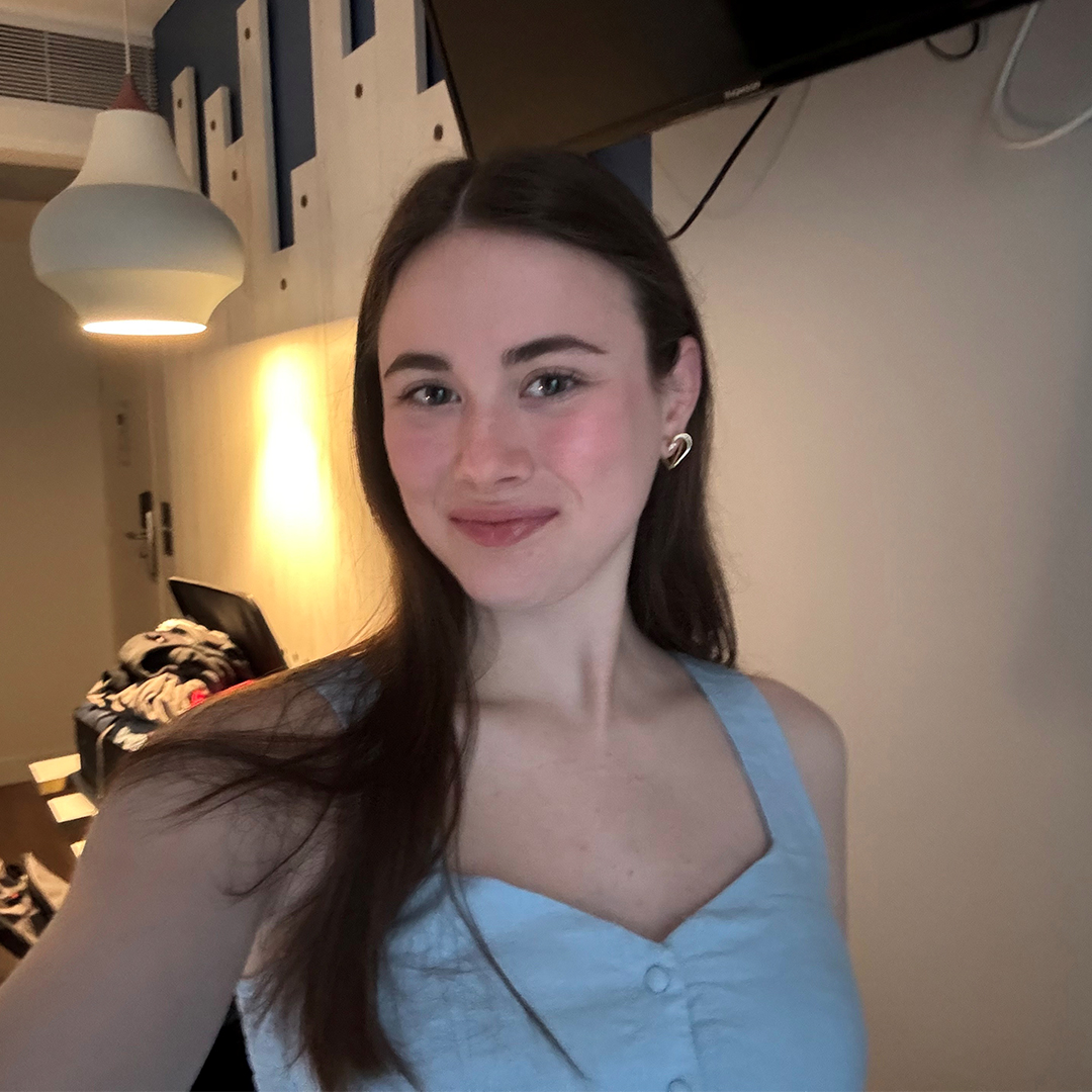Meredith Gelles smiling indoors in a light blue top with long dark hair.