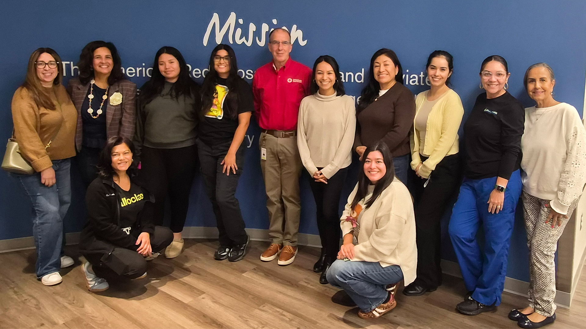 Members of the Philadelphia National Association of Hispanic Nurses (NAHN) stand with Ned Bloom, American Red Cross senior volunteer specialist, inside a facility with an American Red Cross logo on the wall.