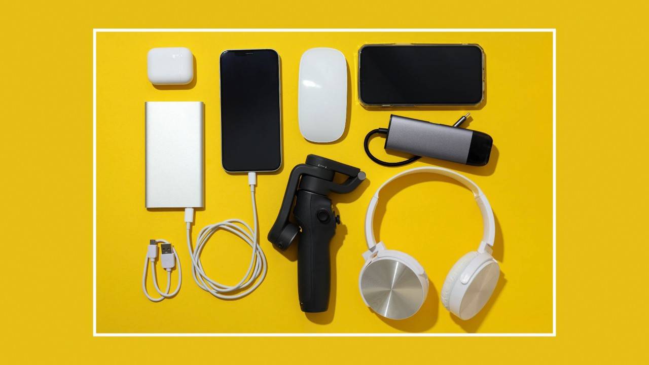 Photo illustration of various common rechargeable electronic devices neatly arranged on a flat surface, including a yellow power bank, smartphones, a power adapter, a charging dock, cables, and headphones.