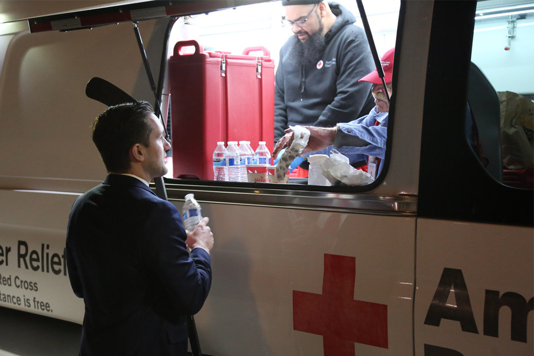 Photo of Red Cross volunteer handing a water bottle to a man through the window of an emergency response vehicle.